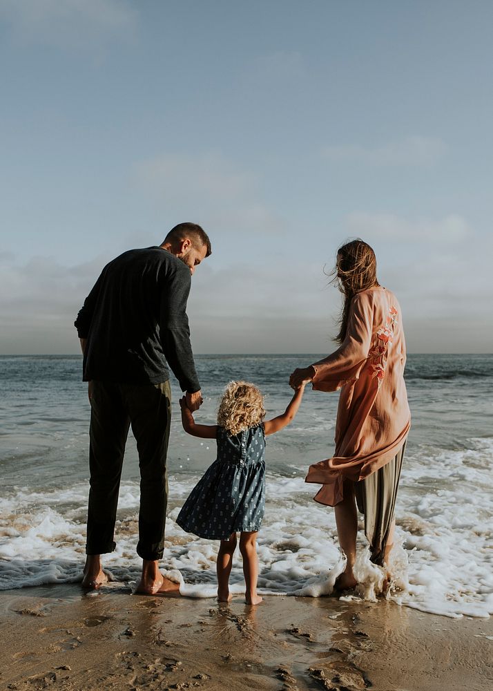 Parents holding daughter's hand at the beach text space 