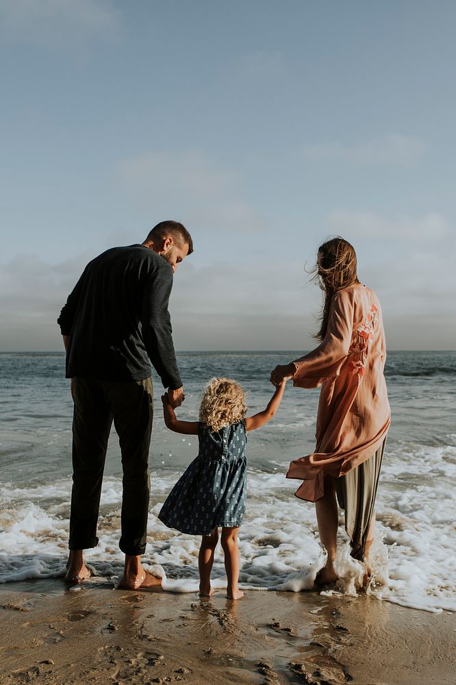 Parents holding daughter's hand at the beach blank space 