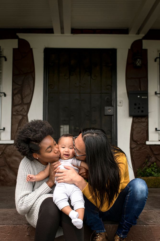 Happy diverse parent kissing their son in front of the house during covid19 lockdown