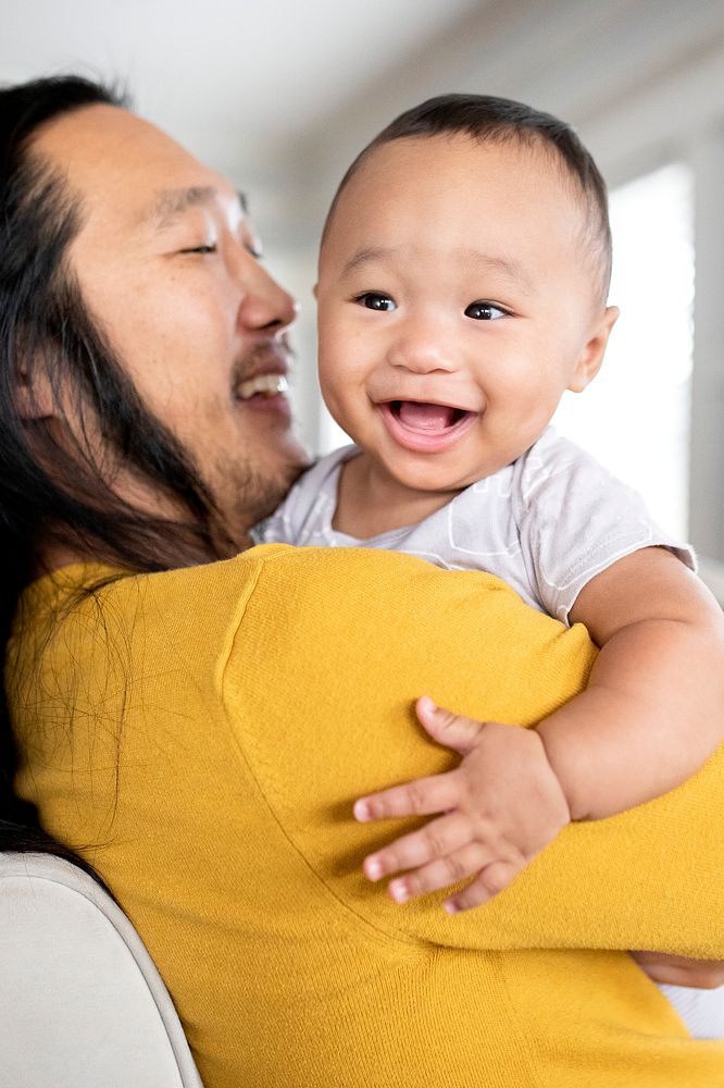 Cheerful Asian American father hugging his baby