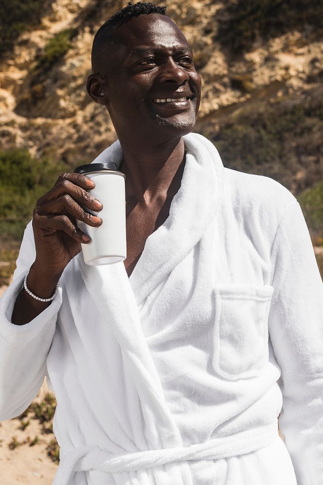 African American senior man in a bathrobe drinking coffee at the beach