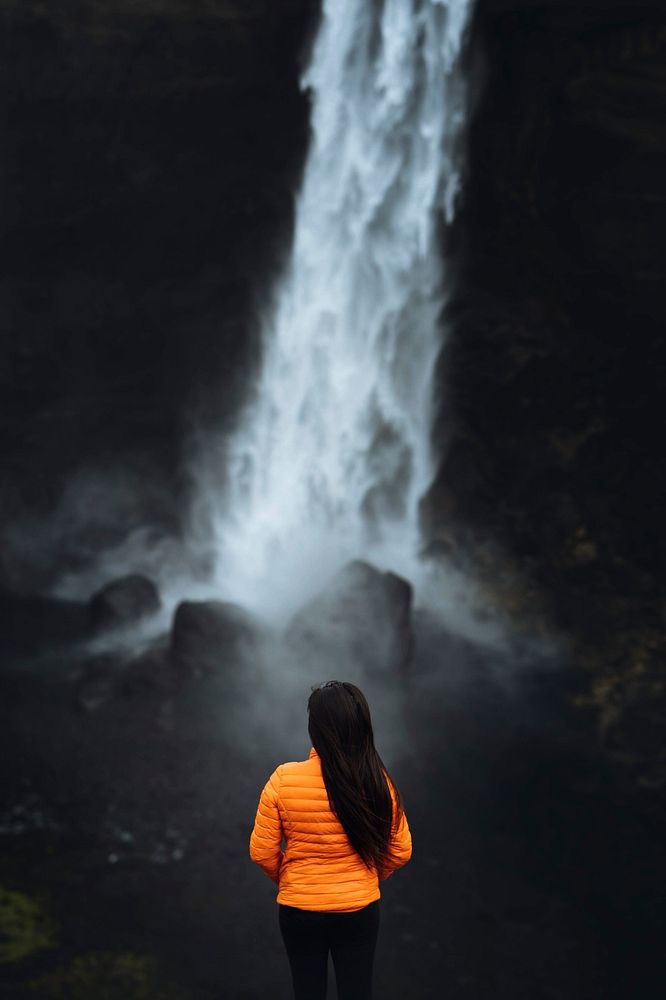 Woman in an orange jacket at the Haifoss waterfall, Iceland