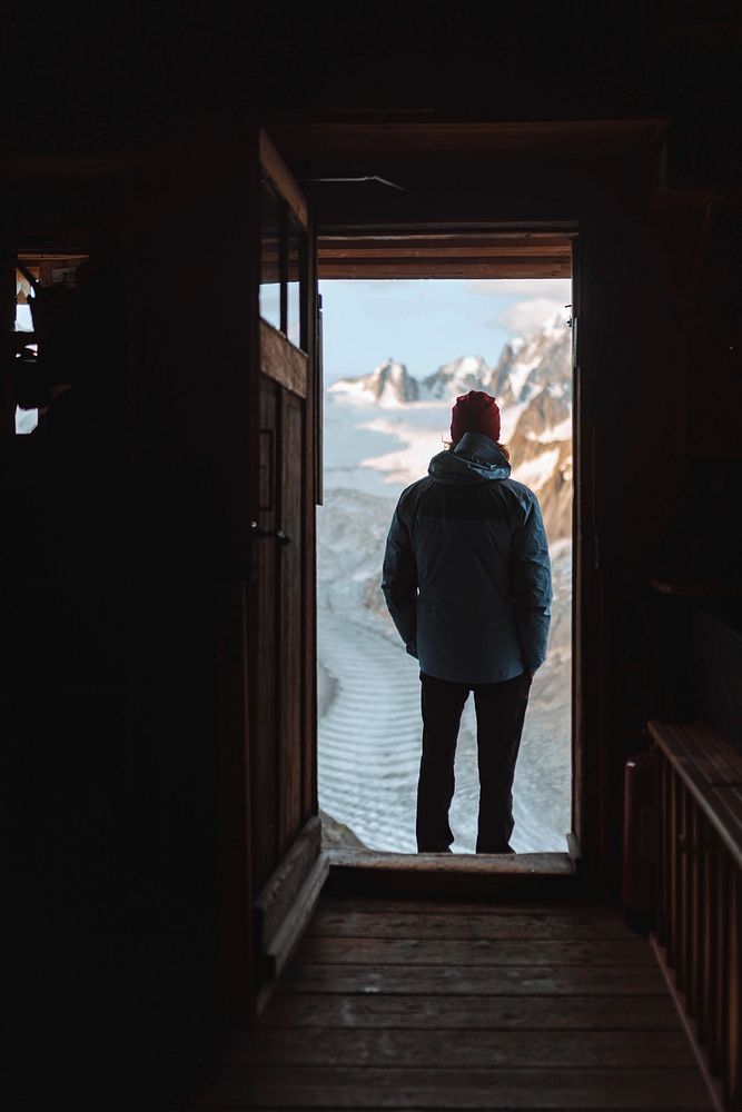 Man standing in a wooden cabin looking at Mont Blanc massif