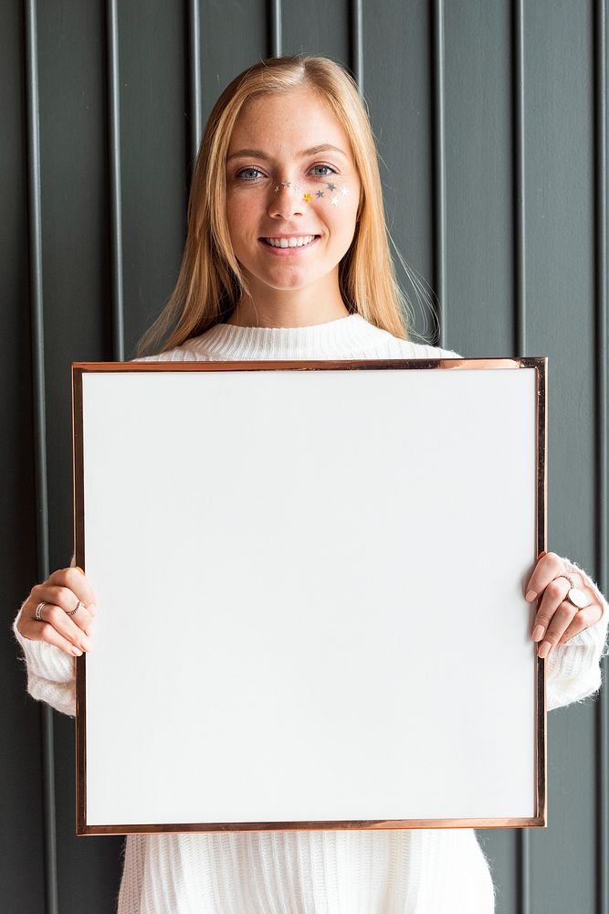 Woman in a white sweater holding a wooden frame