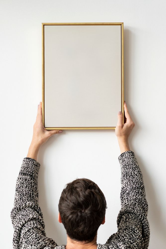 Woman in a black sweater hanging a wooden frame on a white wall