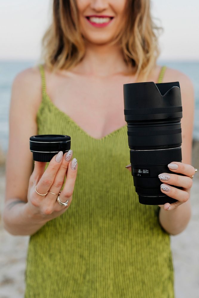 Cheerful woman holding digital camera lenses at the beach