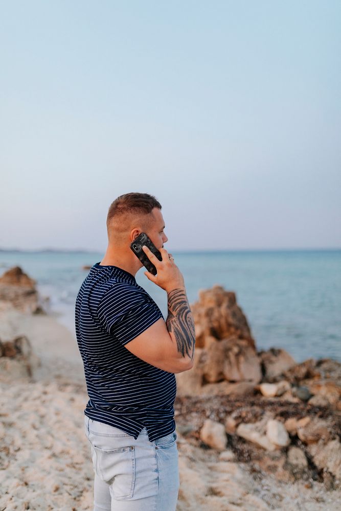Tattooed man talking on a phone at the beach