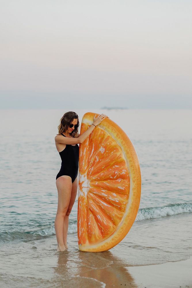 Girl in a black swimsuit with an orange inflatable float at the beach