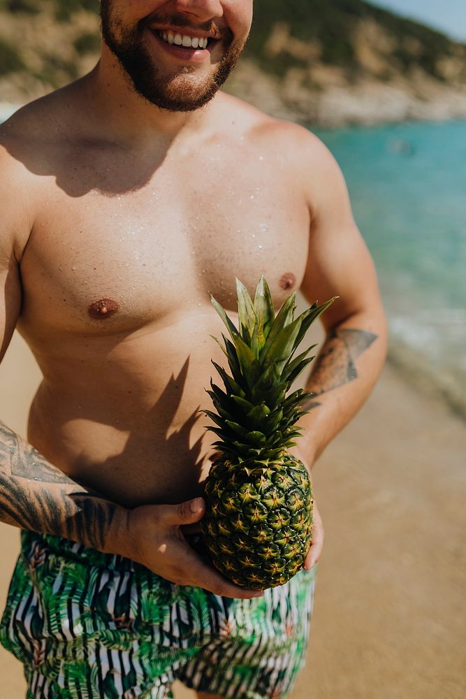 Tattooed man holding a pineapple at the beach