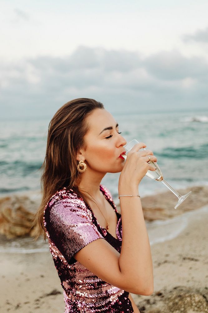 Woman in a pink dress having a glass of champagne at the beach