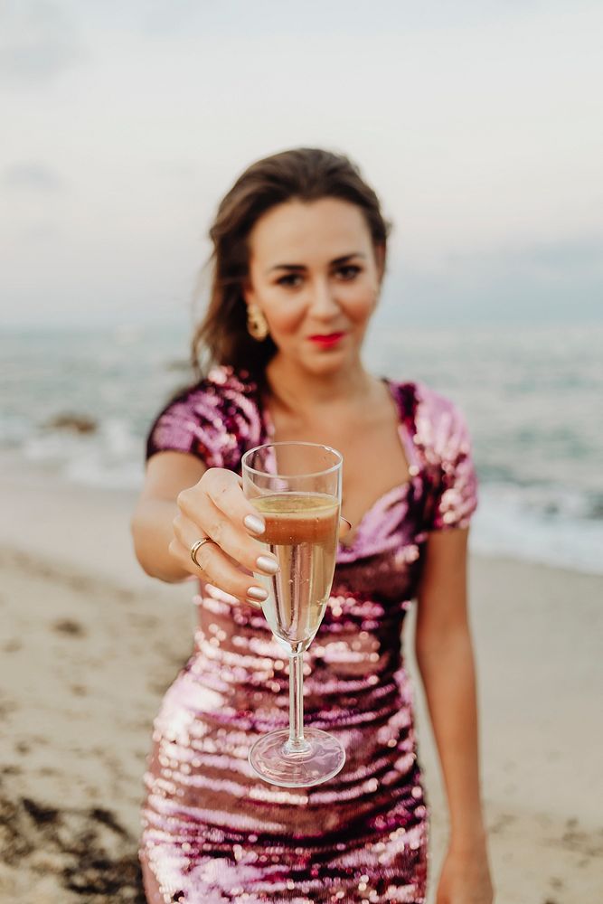 Woman in a pink dress having a glass of champagne at the beach