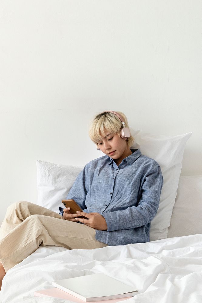 Blond haired Asian woman listening to music in a white bed
