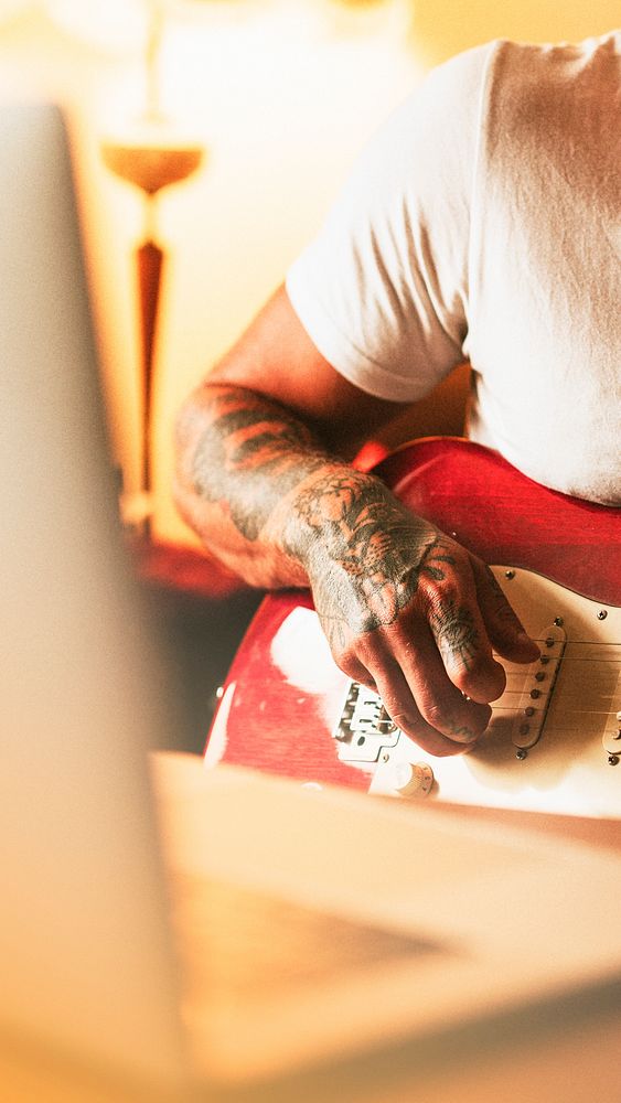 Tattooed man practicing electric guitar at home