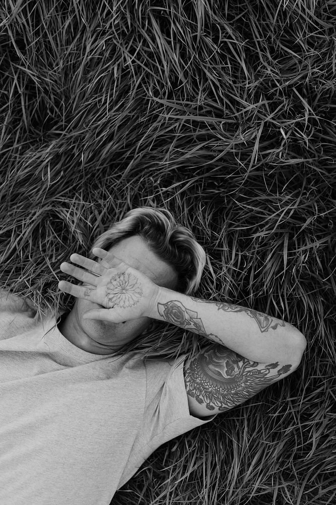 Tattooed man lying on grass, gray photo