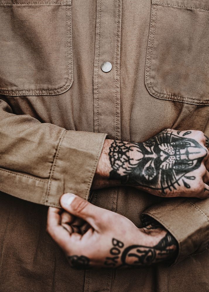 Tattooed man buttoning brown shirt closeup