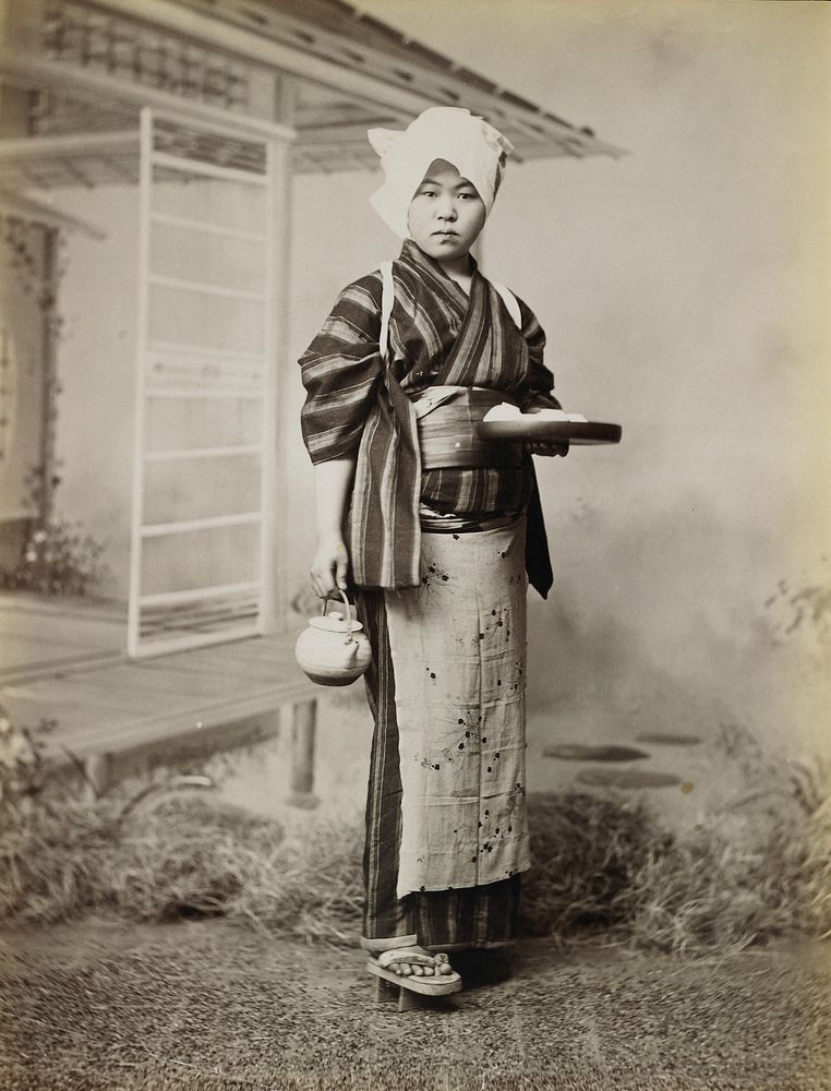 portrait of a woman wearing a striped kimono, white cloth on her head, flowered apron, and "geta" sandals, holding a round…