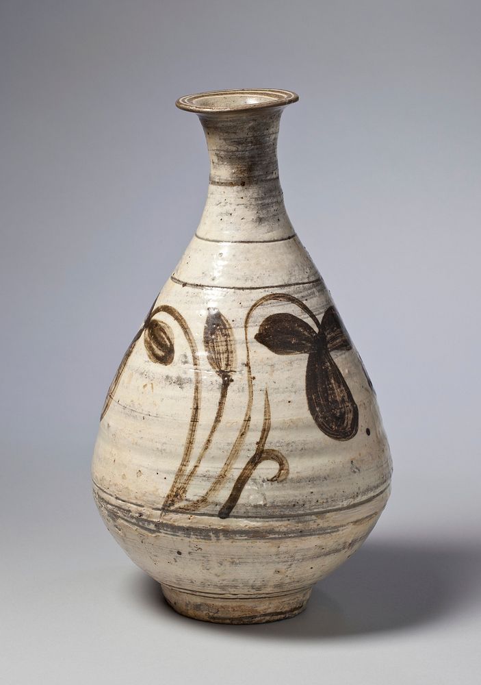 White bottle with looping floral decoration on body; incised lines around base of neck and body; narrow neck, wide body…