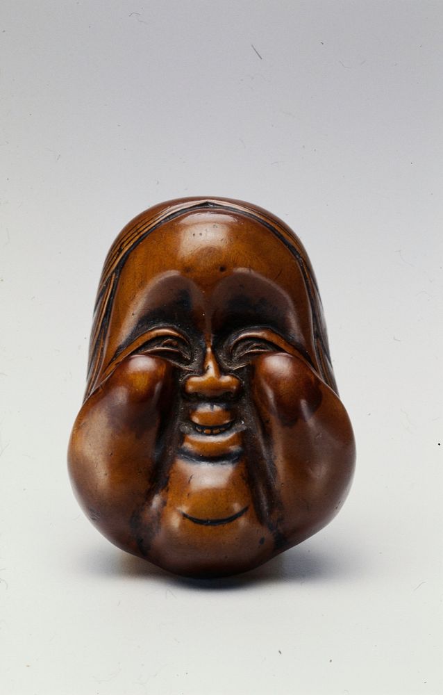 Top side carved with smiling mask with protruding cheeks and forehead; bottom side carved with female genitalia and hand.…