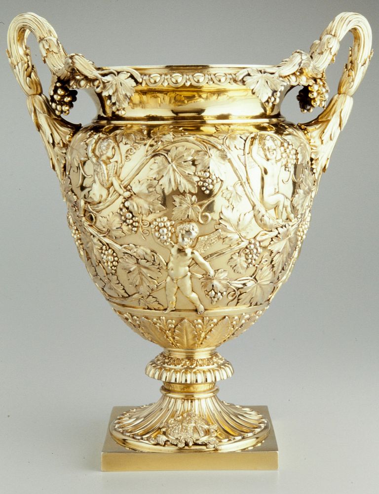 classical vase form; on square base with fluted pedestal feet; cast coat of arms; decorated with putti amidst scrolling…