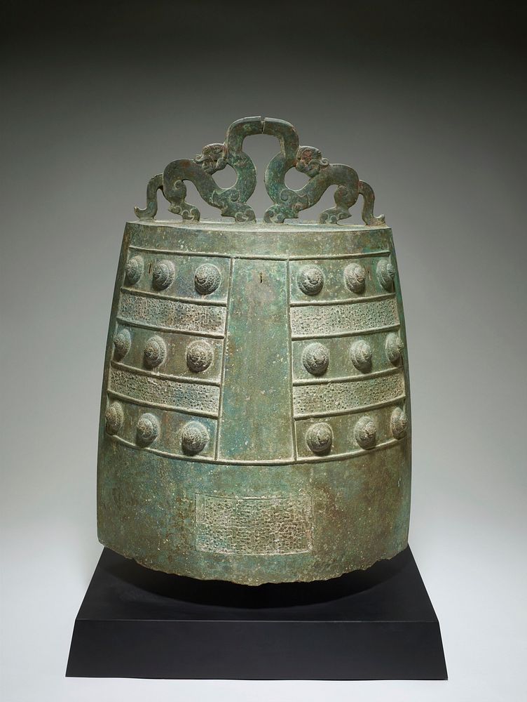 bronze budhist temple bell; tall football shaped body with flat top; two dragons turned away from each other form hanger at…