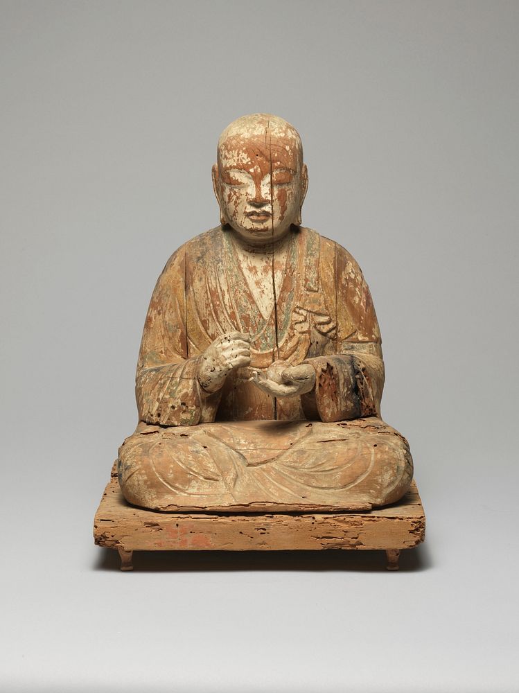 Buddha seated with legs folded and feet over knees; PR hand held in loose fist; PL hand open, gently cradling round object;…