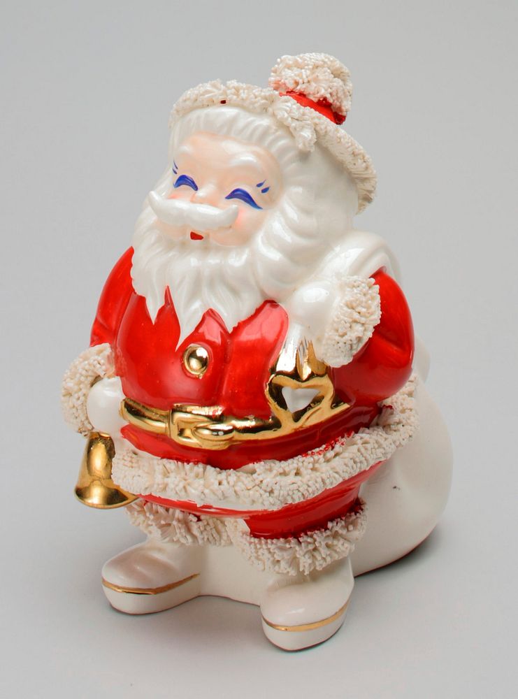 standing Santa Claus figure with gold belt, gold button and gold bell in PR hand; very large, lumpy white sack over PL…