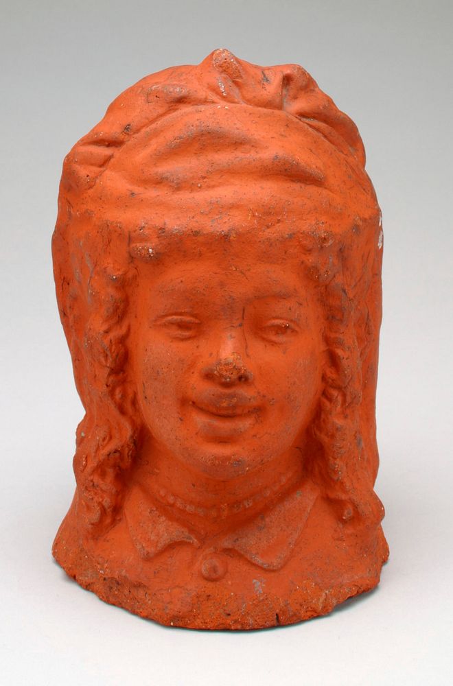 ceramic bust of a woman covered in reddish pigment; wearing a hat, a collar and beads; smiling; curly hair. Original from…