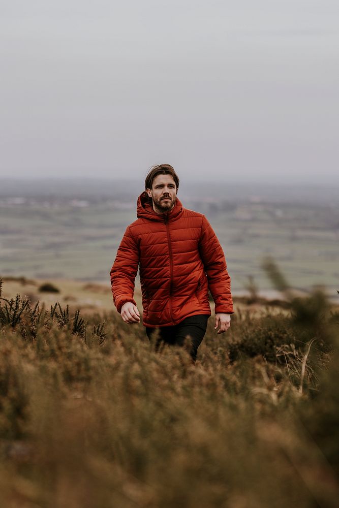 Man wearing orange puffer jacket, walking on hill