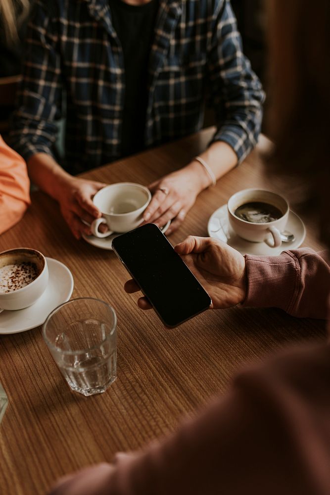 Man holding smartphone, coffee cups on table