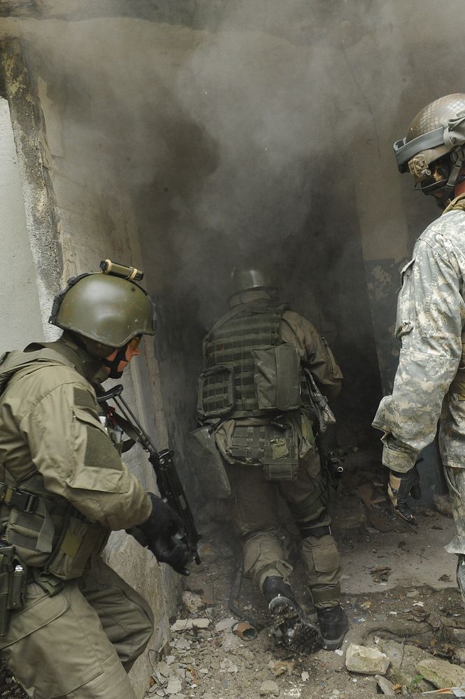 Polish special operations soldiers with the 1st Special Forces Regiment enter a building after breaching a door while a U.S.…