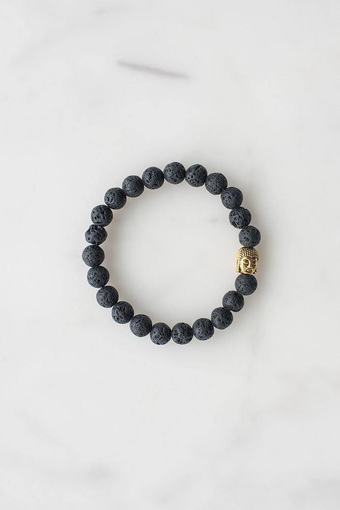 Far away view of black stone looking beaded bracelet with gold buddha charm for men.