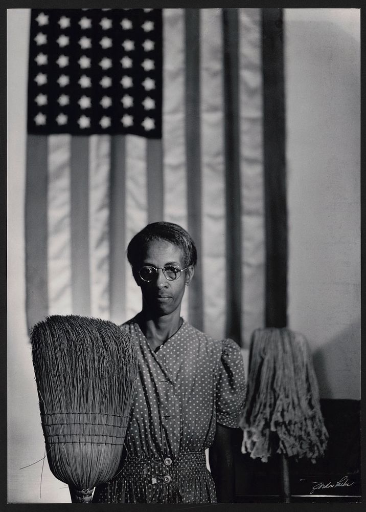 American Gothic. Photograph shows Farm Security Administration employee Ella Watson standing with mop and broom in front of…