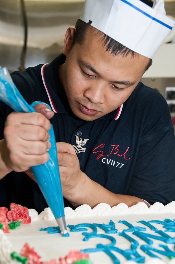 U.S. Navy Culinary Specialist 2nd Class Edgar Baldov decorates a cake aboard the aircraft carrier USS George H.W. Bush (CVN…