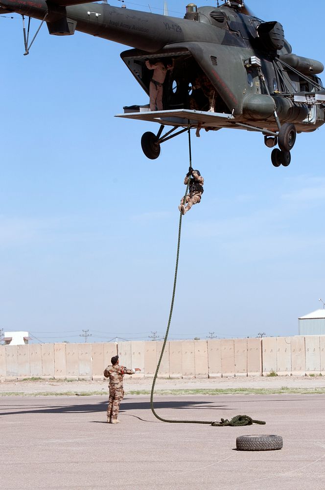 An Iraqi Counter Terrorism Service student fast-ropes from a helicopter, while his instructor watches from the ground at…