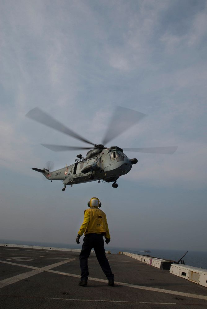 U.S. Navy Aviation Boatswain's Mate (Handling) 3rd Class Eddie Delacruz signals an Indian Navy UH-3H helicopter to take off…