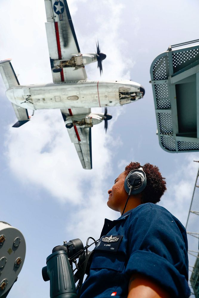 U.S. Navy Boatswain's Mate 3rd Class Briana Lewis stands starboard life-buoy watch on the fantail while a C-2A Greyhound…