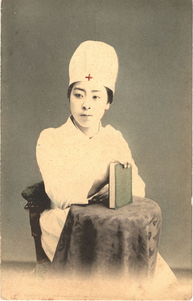 Japanese Nurse Holding a Book. Color photo of a Japanese nurse in her nursing uniform holding a book on a table and sitting…