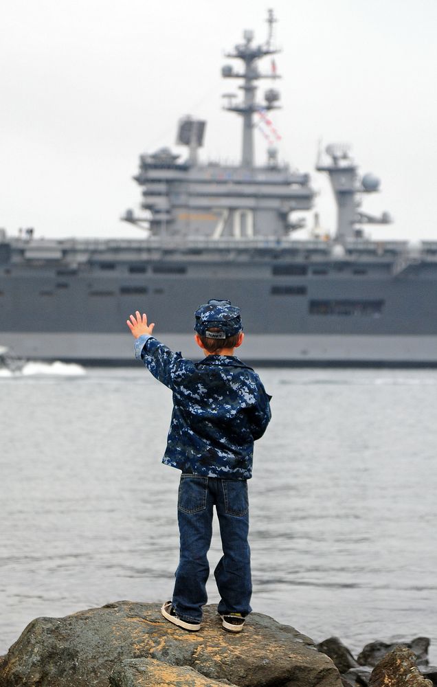 The son of U.S. Navy Electrician's Mate 1st Class Randall White waves to his father's ship, the aircraft carrier USS Carl…