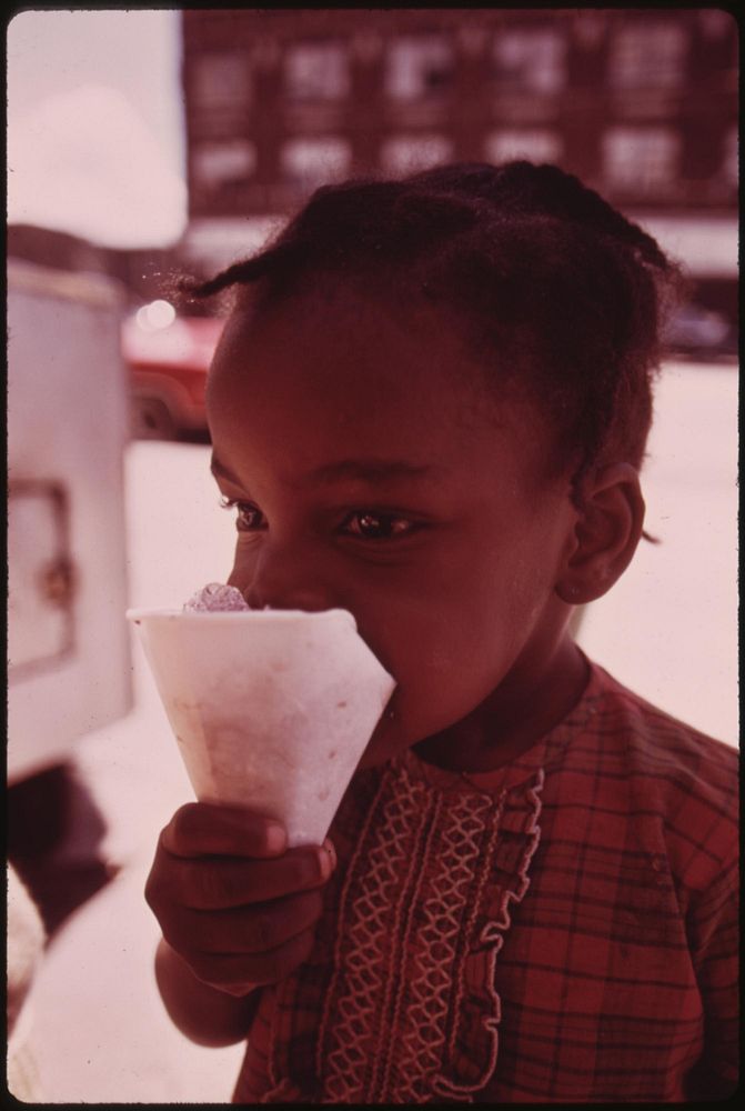 Black Ghetto Child Savors A Snow Cone Just Received From A Sidewalk Vendor On Chicago's West Side, 06/1973. Photographer:…