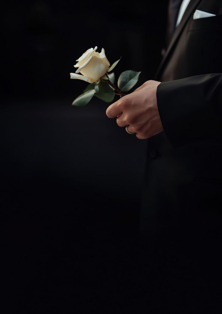 photo of hand in suit put white rose on a funeral casker.  