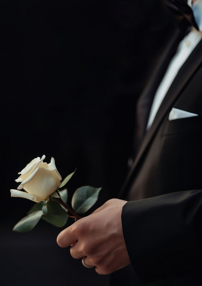 photo of hand in suit put white rose on a funeral casker.  