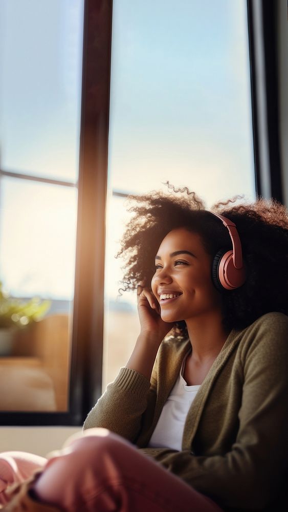 photo of A black woman sitting on a couch happy with wearing headphones in a minimal living room. 