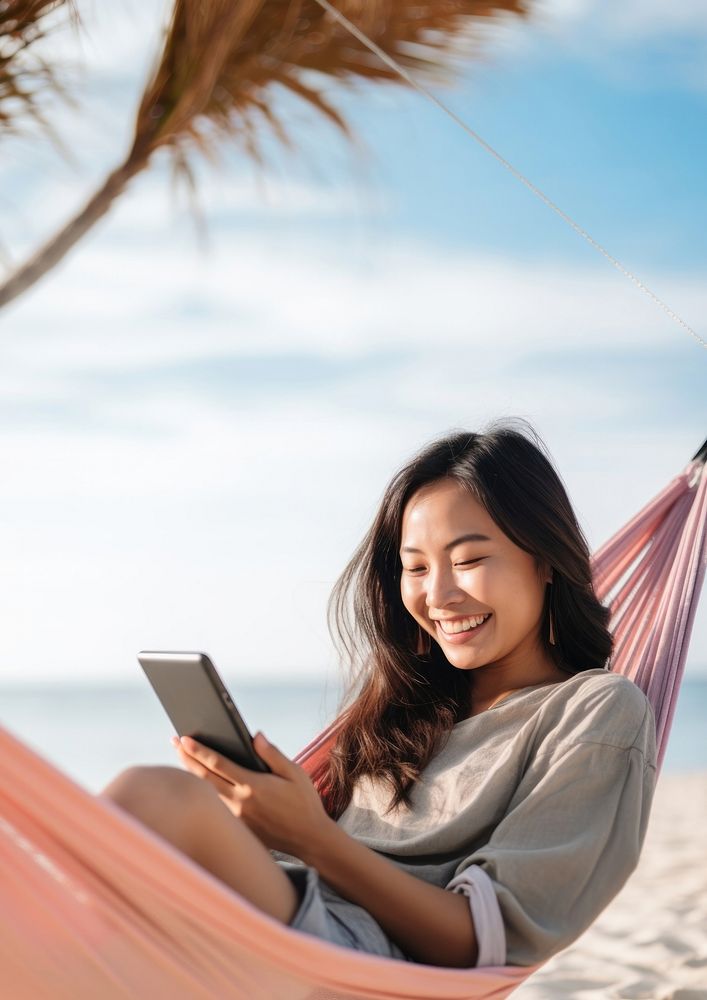 Happy traveler asian woman using mobile phone and relax in hammock on beach. 