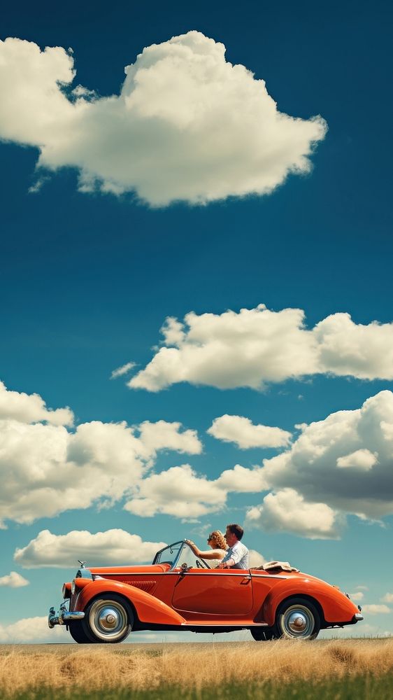 Photo of couple driving in red vintage car on countryside. 