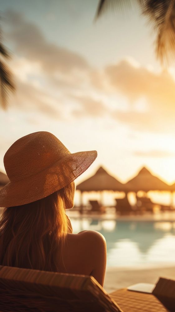 Woman relaxing by the pool in a luxurious beachfront hotel resort at sunset enjoying perfect beach holiday vacation.  