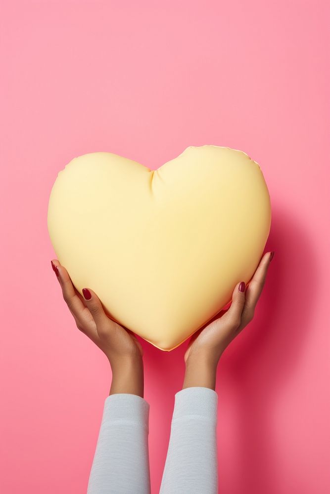 Hand holding big heart pillow yellow pink celebration. AI generated Image by rawpixel.