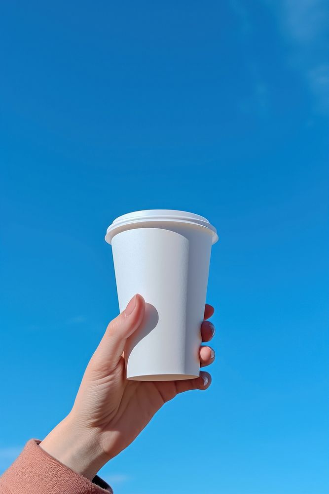 Hand holding disposable coffee cup against a clear sky mug day refreshment. AI generated Image by rawpixel.