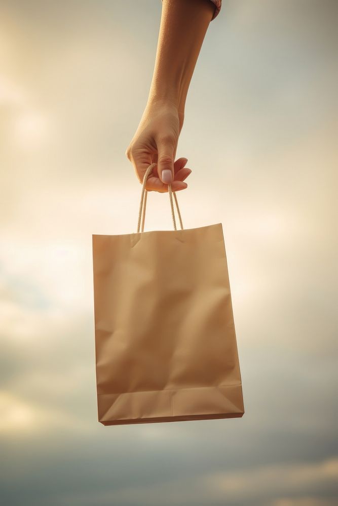 Hand holding a paper bag handbag sky consumerism. AI generated Image by rawpixel.