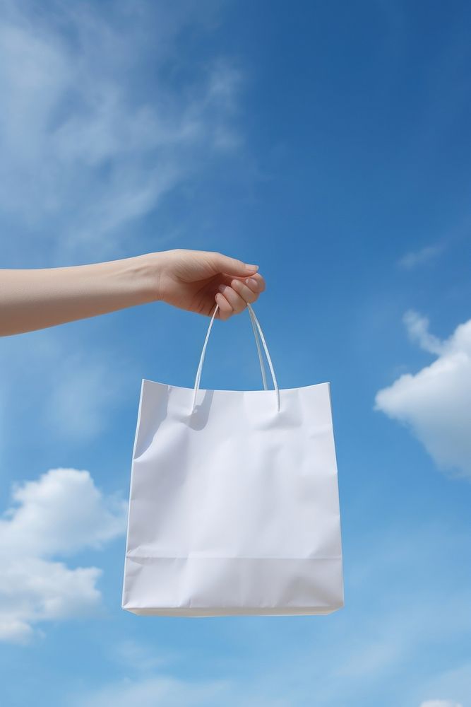 Hand holding a paper bag handbag sky consumerism. AI generated Image by rawpixel.