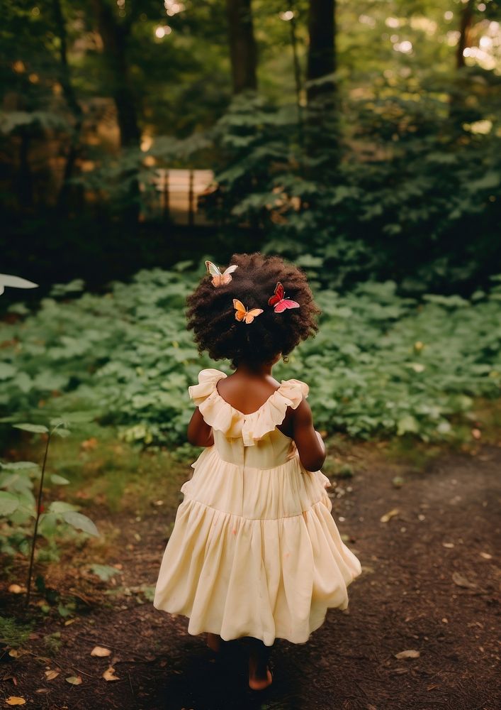 A 2 years old black girl wearing cream dress and a colorful butterflies hair clip in the green yard photography portrait…